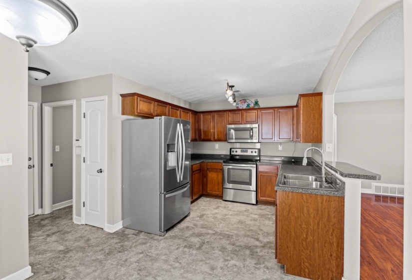 U-shaped kitchen featuring wood cabinetry, stainless steel appliances, dark countertops, and a double basin sink with a high-arc faucet