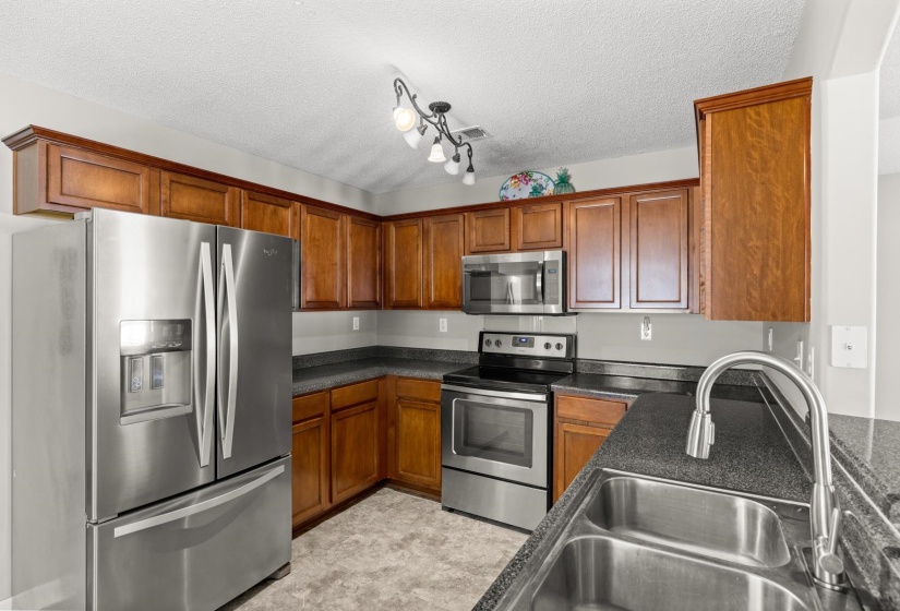 Kitchen featuring stainless steel appliances, wood cabinetry, dark countertops, and a double basin sink with a high-arc faucet