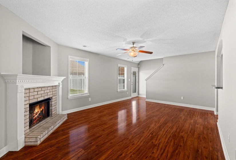 Living area featuring rich wood-finish flooring, a brick fireplace with a white mantel, and a ceiling fan with integrated lighting