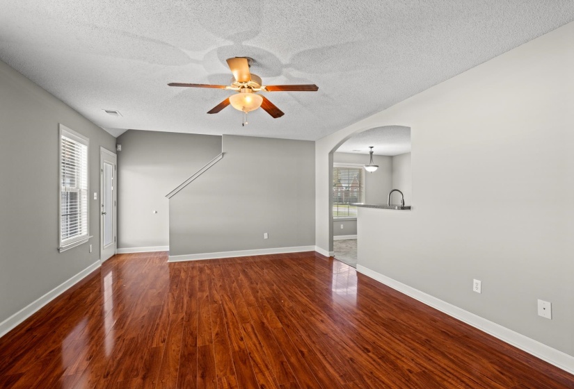 Spacious living area featuring rich wood-finish flooring, a ceiling fan with integrated lighting, and neutral wall tones