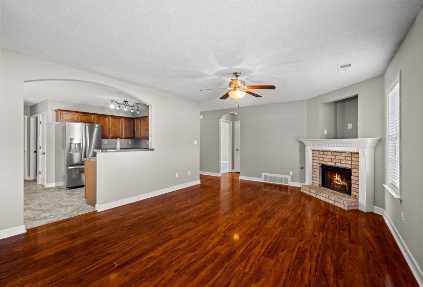 Spacious living area featuring wood-finish flooring, a brick fireplace with a white mantel, and a ceiling fan