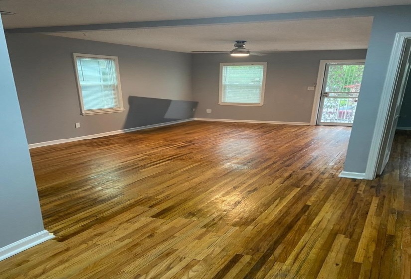 Spacious room featuring wood-finish flooring, light grey painted walls, white trim, and a ceiling fan