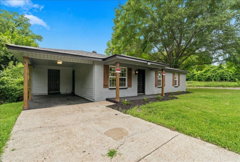 Gray brick and siding exterior featuring a covered carport, wood-finish window shutters, and a concrete driveway