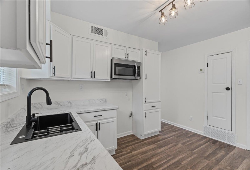 Modern kitchen featuring white cabinetry with matte black hardware, a stainless steel microwave, and wood-finish flooring