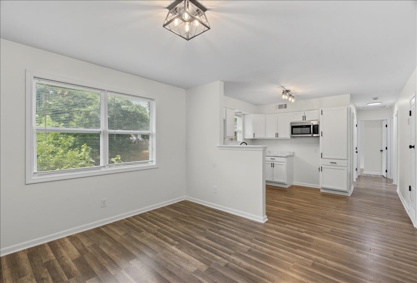 Open-concept living space featuring wood-finish flooring, white walls, and contemporary light fixtures