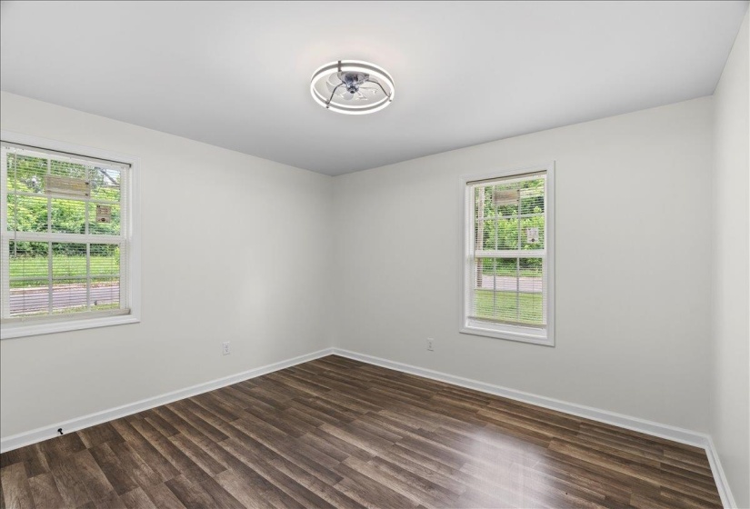 Spacious room featuring wood-finish flooring, two large windows, white walls, and a modern ceiling light fixture