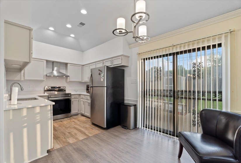 Modern kitchen featuring light-toned cabinetry, stainless steel appliances, wood-finish flooring, and a sliding glass door with vertical blinds