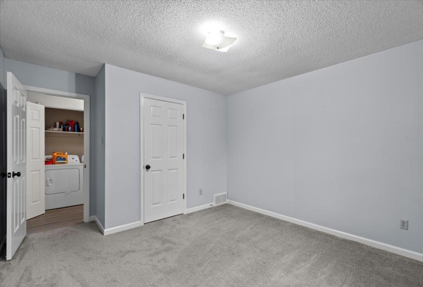 Light gray wall paint with white trim, gray carpet flooring, and a white six-panel door with a black knob
