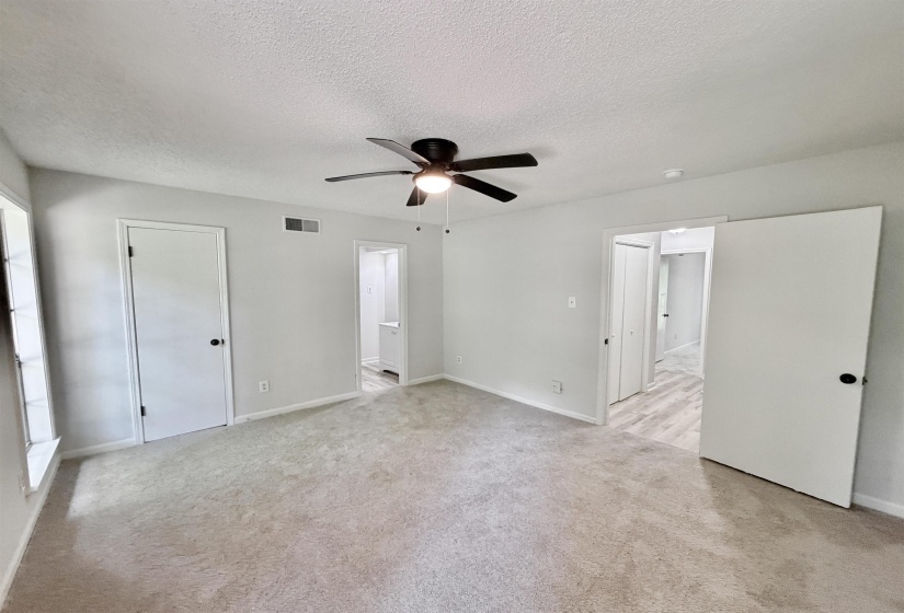 Spacious carpeted room featuring a ceiling fan with integrated lighting, white interior doors with dark hardware, and light-toned walls