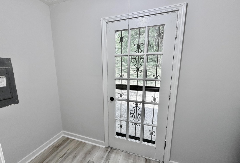 White framed glass-panel door with decorative iron inserts, wood-finish flooring, white baseboards, and light gray wall paint