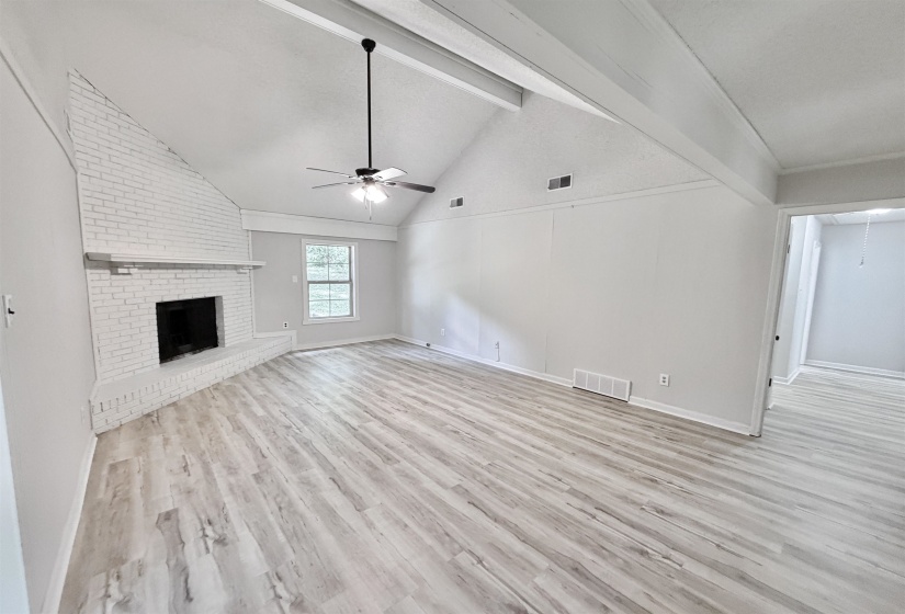Living area featuring a painted brick fireplace, vaulted ceiling with exposed beams, wood-finish flooring, and a ceiling fan
