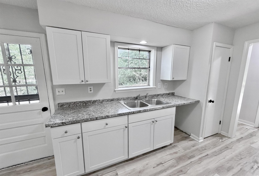 Bright kitchen area featuring white shaker-style cabinetry, a double basin stainless steel sink, and speckled gray countertops