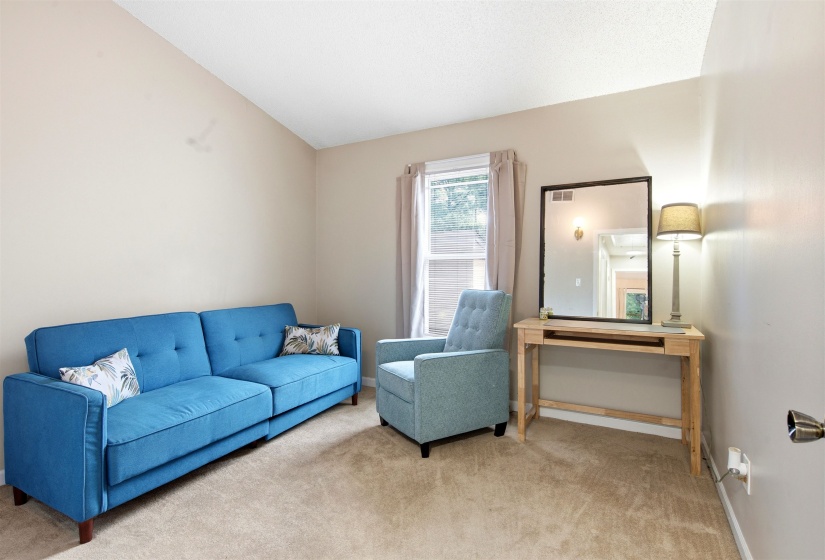 Vaulted ceiling room with neutral-toned walls, carpeted flooring, and a large window with drapes