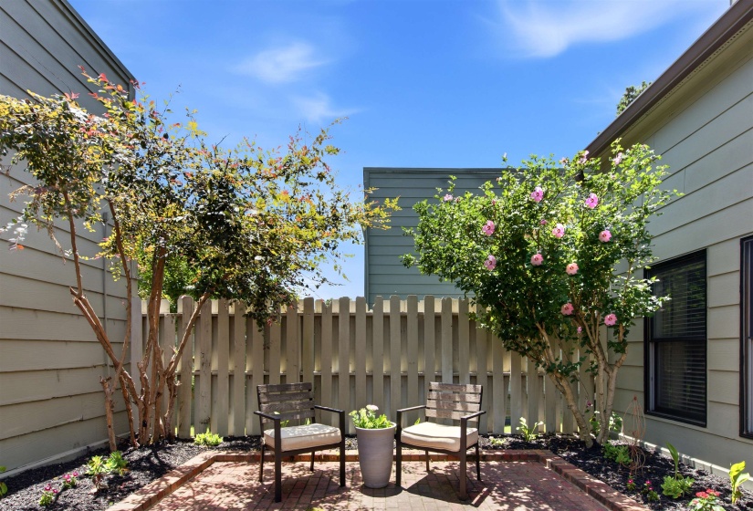Private patio featuring brick pavers, a wooden privacy fence, mature trees, and planted landscaping beds