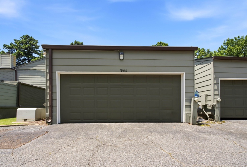 Attached two-car garage with a panel door, featuring a wall-mounted exterior light fixture and an adjacent parking surface