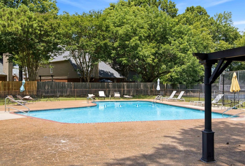 Resort-style pool area featuring a perimeter fence, ample sundeck, and lush surrounding trees