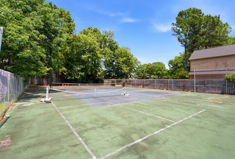 Private tennis court with a chain-link fence surround and mature perimeter trees