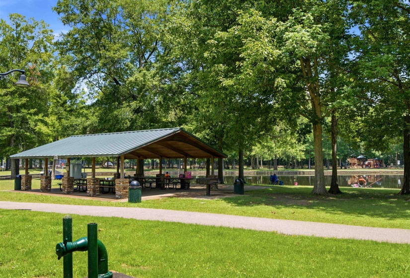 Open-air pavilion featuring a green metal roof, stone-clad support columns, and built-in picnic tables