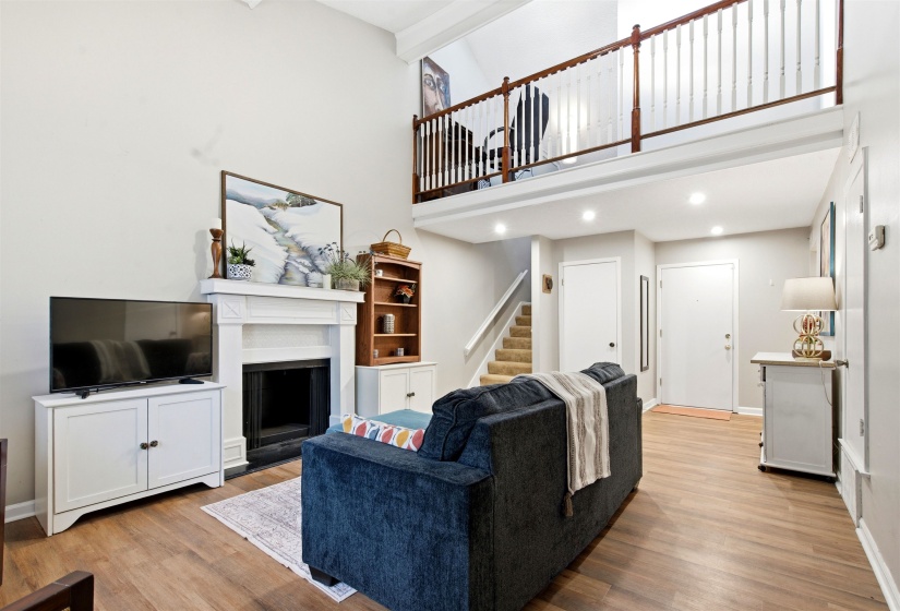 Living area featuring a fireplace with a white mantel, wood-finish flooring, and a second-story loft with a wood and white spindle railing