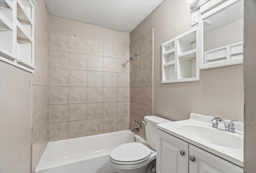 Bathroom featuring a white bathtub, ceramic wall tiling, white vanity with integrated sink, chrome faucet, and white framed medicine cabinet