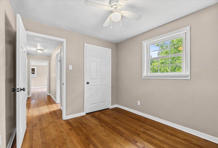 Room featuring wood-finish flooring, a ceiling fan, a window with white trim, and light beige walls