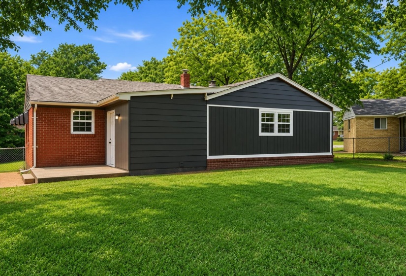 Spacious green lawn surrounding a residence with a red brick facade and dark siding accents