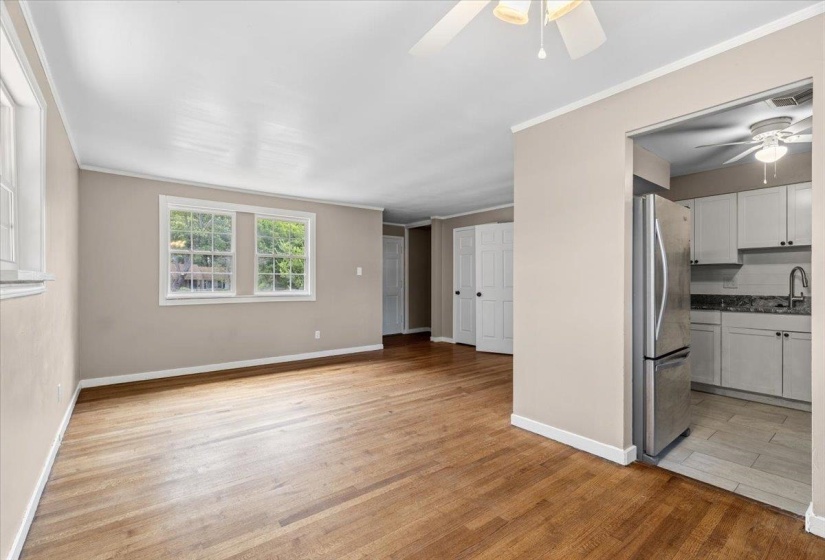 Bright living area featuring wood-finish flooring, neutral paint, multiple windows, a ceiling fan, and an open doorway to the kitchen with stainless steel appliances and stone countertops