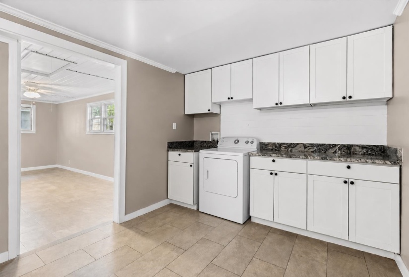 Laundry area featuring extensive white cabinetry, dark stone-finish countertops, and a tile backsplash