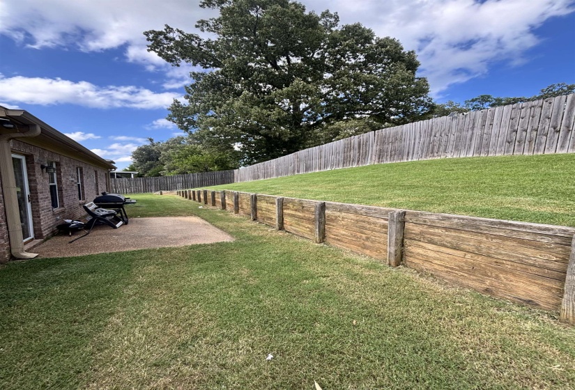 Expansive lawn area featuring a wood retaining wall and a privacy fence
