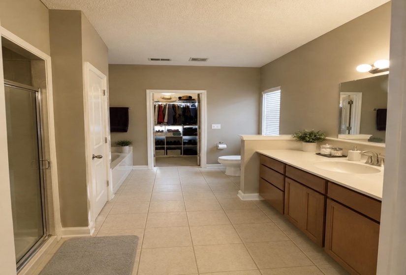 Expansive bathroom featuring neutral tile flooring, a large vanity with an integrated sink, and an enclosed shower