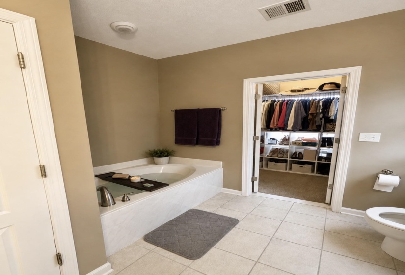 Bathroom featuring a built-in tub with deck-mounted fixtures, light-toned floor tiles, and a neutral wall color
