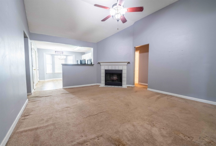 Spacious living area featuring a vaulted ceiling and a ceiling fan with light fixture