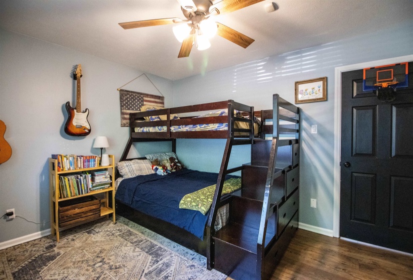 Room featuring wood-finish flooring, a ceiling fan with light fixture, light  wall paint, white baseboards, and a black paneled door