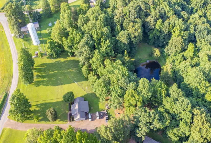 Expansive property featuring a private pond, mature tree coverage, and a residential structure with a dark shingle roof