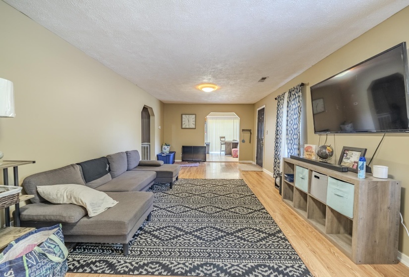 Spacious living area featuring wood-finish flooring, neutral wall tones, and arched doorways