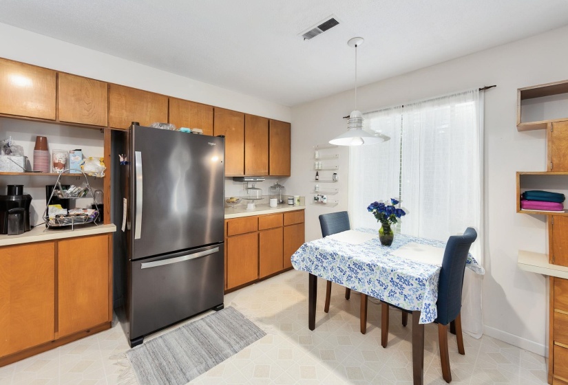 Kitchen featuring a stainless steel refrigerator, wood cabinetry, laminate countertops, and a dining area with a pendant light fixture