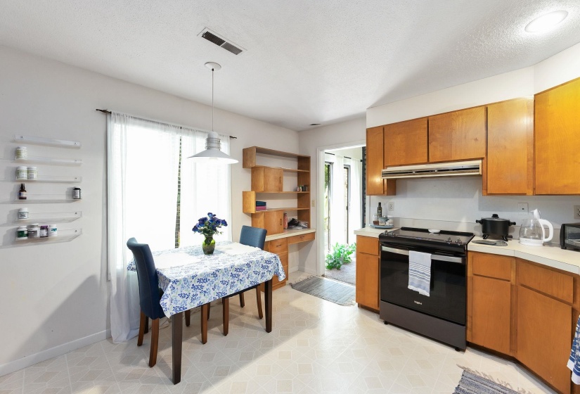 Kitchen and dining area featuring light wood-finish cabinetry, a black range with an overhead vent, and light-toned flooring