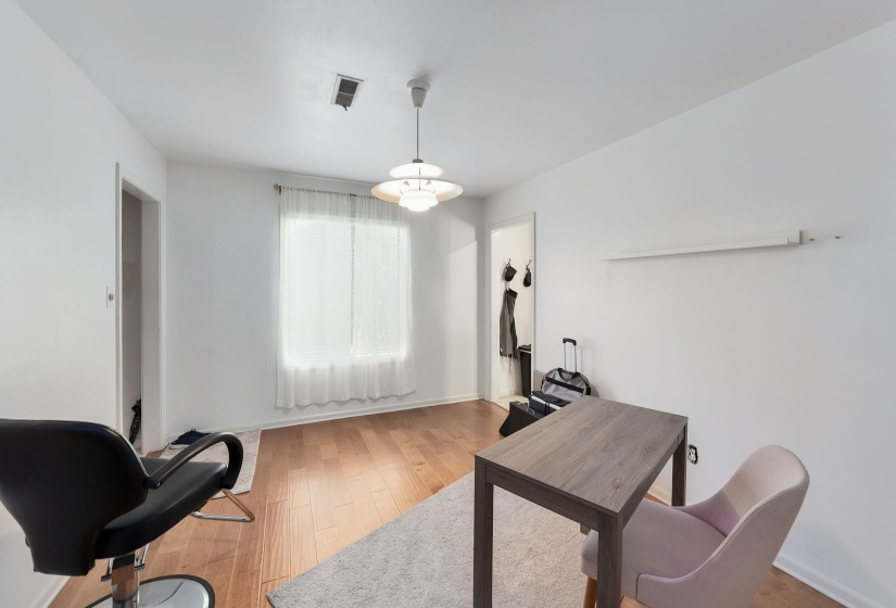 Bright room featuring a window with sheer white curtains, wood-finish flooring, white walls, and a modern tiered ceiling light fixture