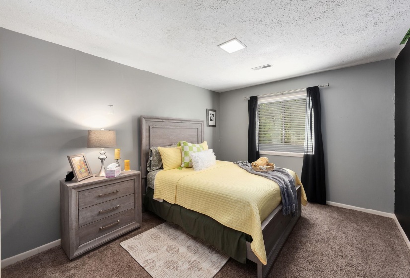 Spacious room featuring neutral gray walls, brown carpet flooring, a window with horizontal blinds and dark drapery, and a contemporary ceiling light fixture