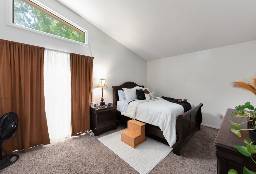 Vaulted ceiling bedroom featuring a high-level triangular window, wall-to-wall carpeting, and light gray painted walls