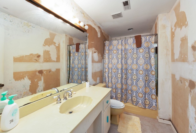 Bathroom featuring a built-in vanity with an integrated sink and chrome faucet, a wall-mounted mirror with overhead lighting, a shower-tub combination with a shower curtain rod, and vinyl flooring