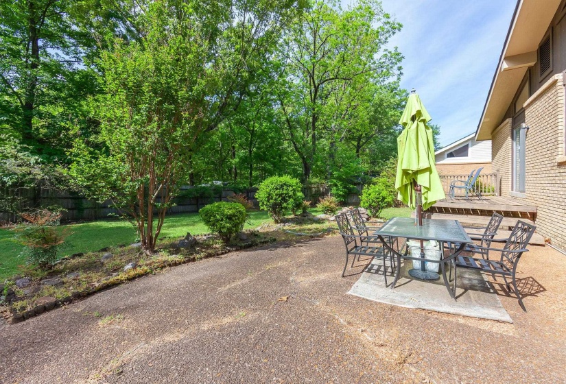 Exterior patio area with a brick facade home, featuring a raised wood deck, a concrete patio, and a gravel-like ground cover