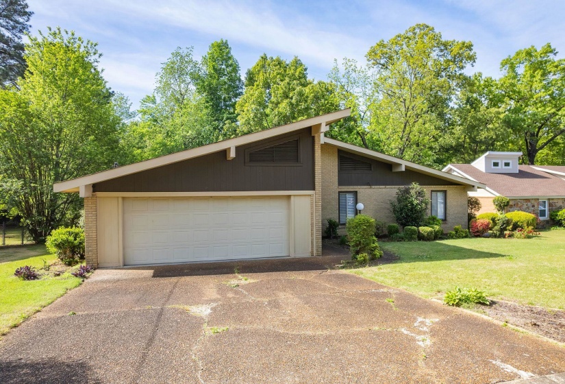 Mid-century modern residence featuring a prominent front-facing garage, brick facade, and a distinctive asymmetric roofline