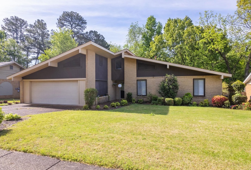 Mid-century modern exterior featuring a brick facade, asymmetrical roofline, integrated garage, manicured front lawn, and mature landscaping