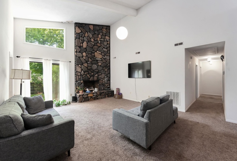 Vaulted ceiling living area featuring a floor-to-ceiling stone fireplace, large picture window, glass panel patio doors, and neutral carpeting