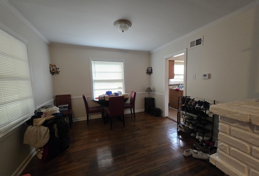 Expansive room featuring rich wood-finish flooring, white crown molding, and two windows with blinds