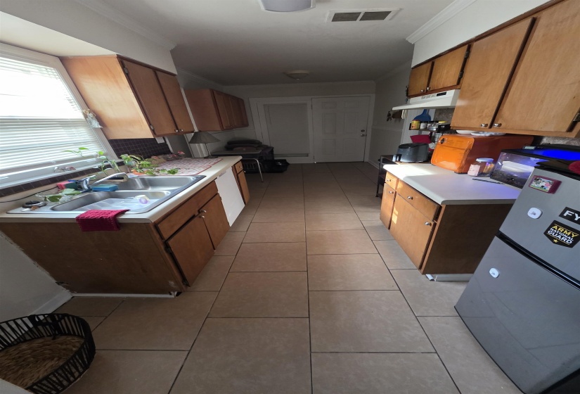 Galley kitchen featuring wood cabinetry, laminate countertops, a double basin stainless steel sink, and light-toned tile flooring