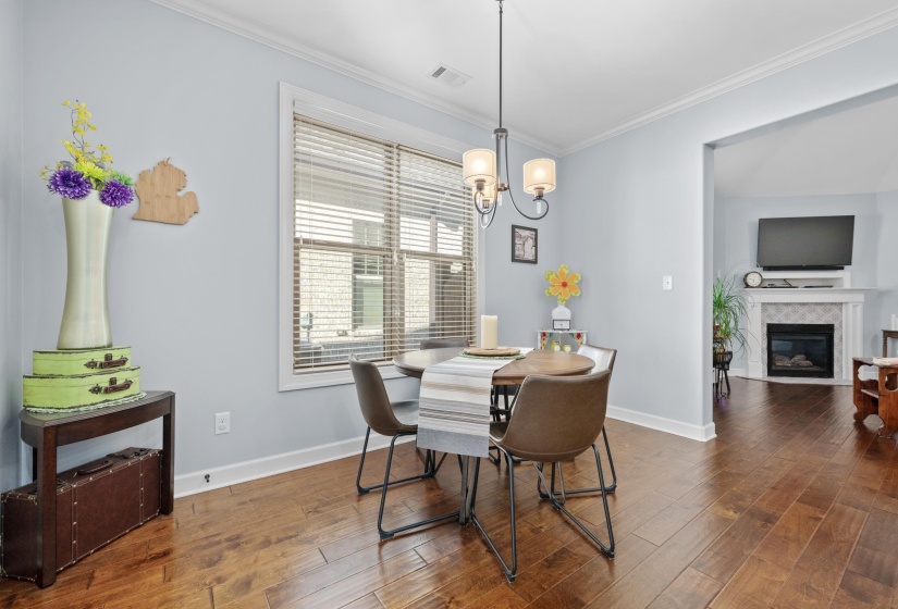 Dining area featuring wood-finish flooring, a contemporary chandelier, a large window with blinds, and an arched doorway opening to a living room with a fireplace
