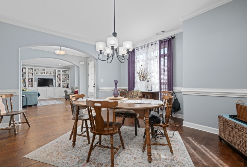 Dining area with rich wood-finish flooring, white crown molding, and a chandelier light fixture