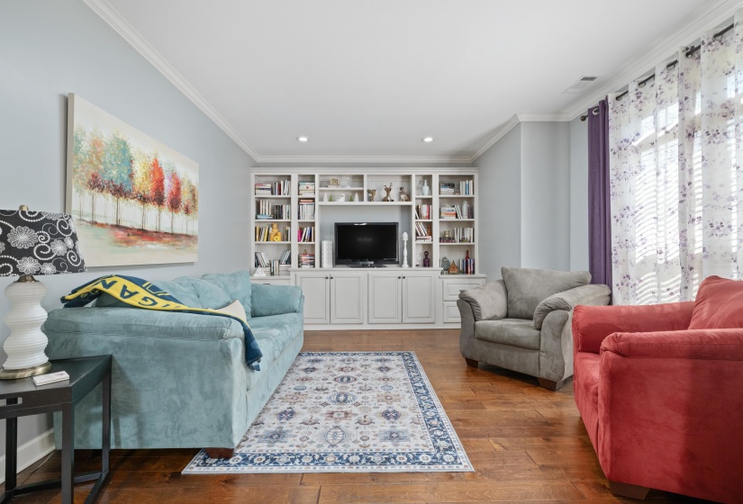 Built-in media center with integrated shelving and lower cabinetry, recessed lighting, crown molding, wood-finish flooring, and natural light from large windows
